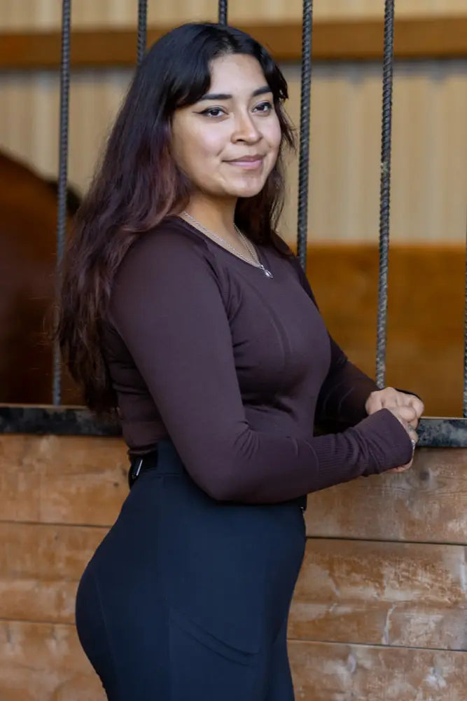 A woman wearing a seamless upf 30 sun protection brown baselayer top and dark blue high waisted pants