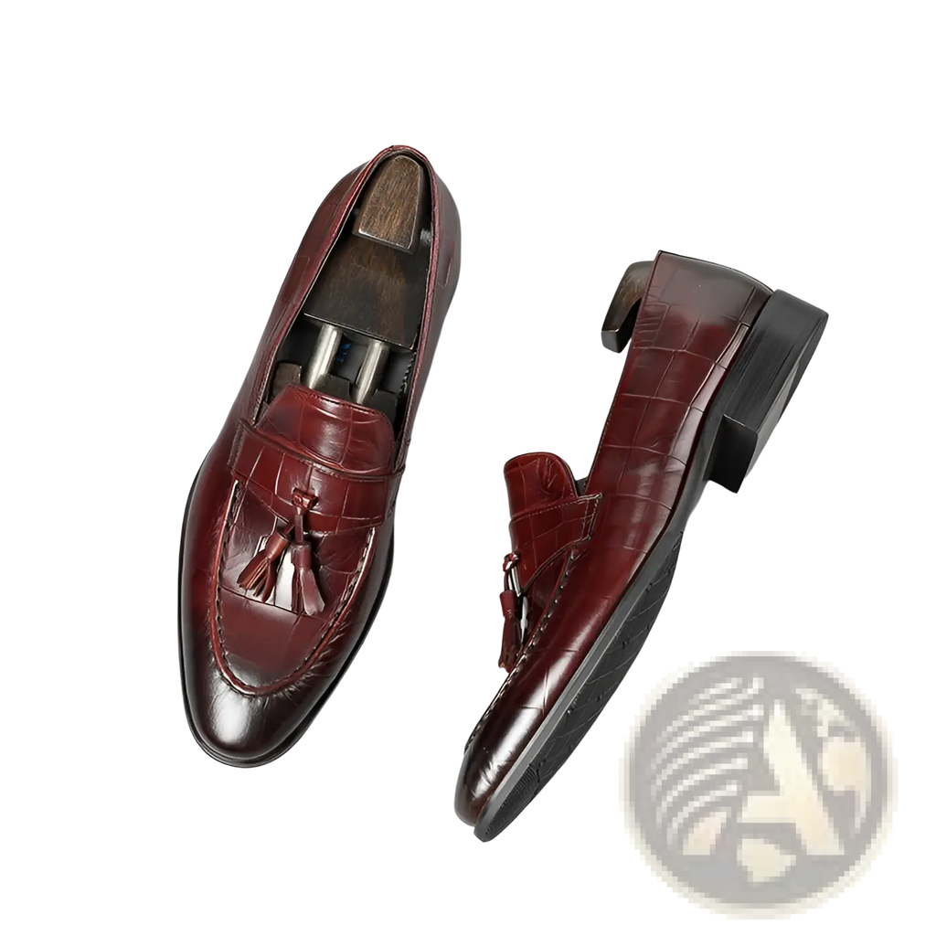 Burgundy crocodile embossed leather tassel loafers with polished finish and black rubber soles shown from the back