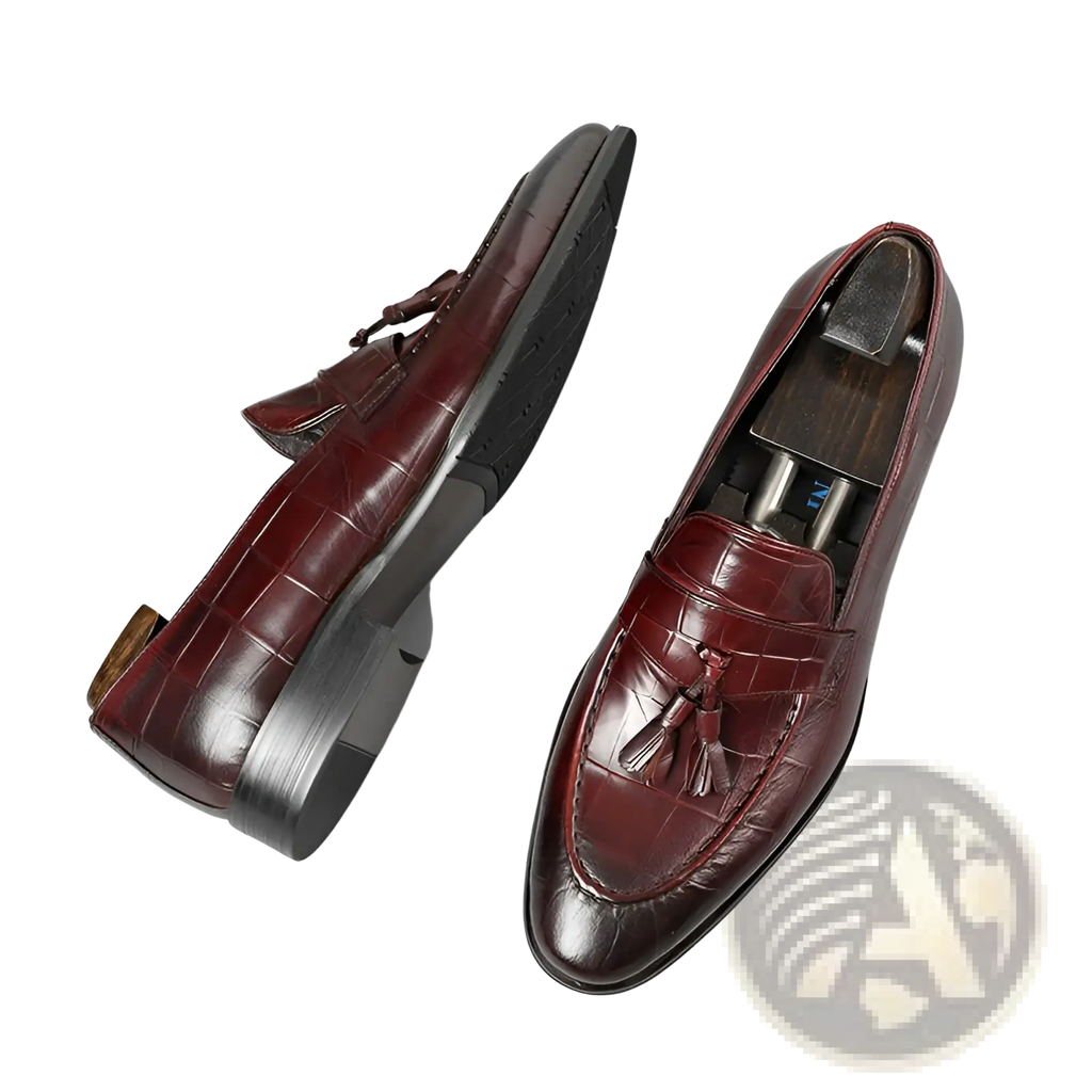 Burgundy crocodile embossed leather tassel loafers with a polished finish and black rubber soles