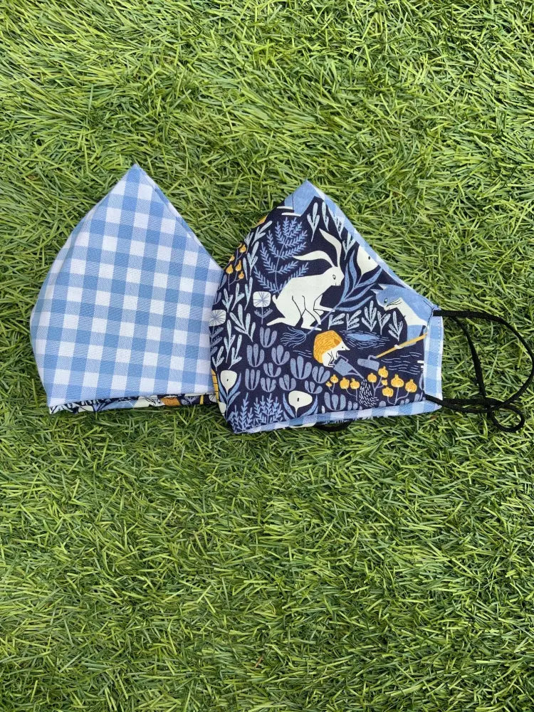 Two reversible cotton face masks in blue gingham and navy with white rabbits and yellow flowers patterns