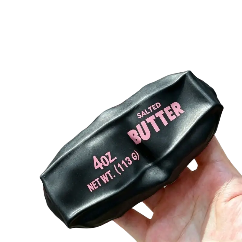 Black salted butter stick asmr sensory squishy toy wrapped in glossy plastic with pink salted butter 4oz text