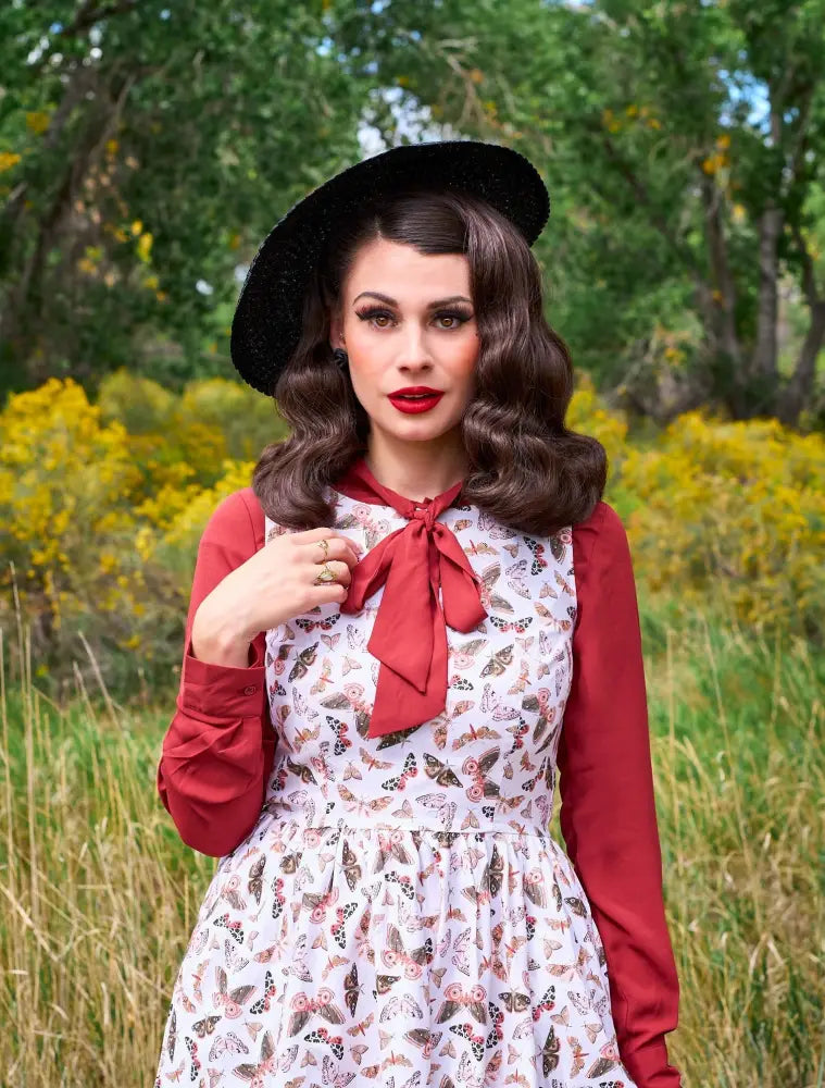 White vintage-inspired cotton midi dress with delicate butterfly print and bold red bow accent at the neckline with long sleeves