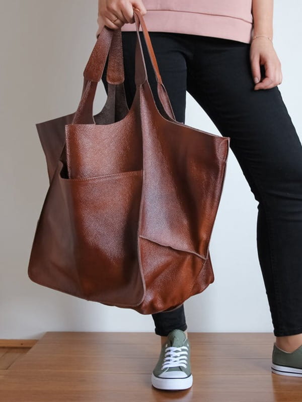 A brown leather tote bag with a textured surface and two sturdy handles designed as a large capacity soft slouchy shoulder bag.