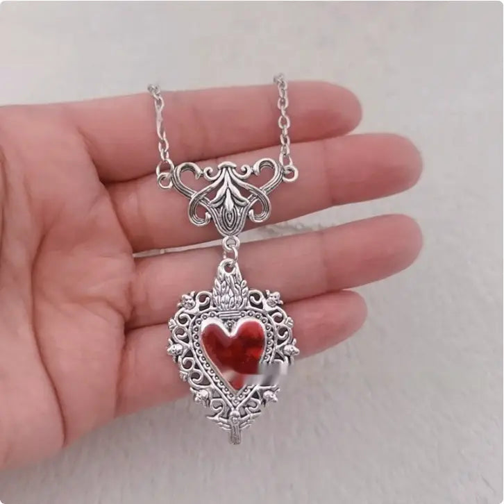 Vintage silver filigree heart pendant necklace with a vibrant red enamel center is displayed.