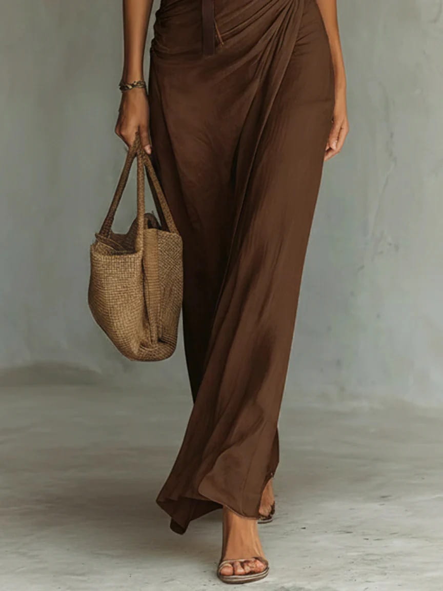 a sleek brown satin cowl neck resort maxi dress paired with a woven beige straw tote bag featuring sturdy handles and a slightly slouched casual shape