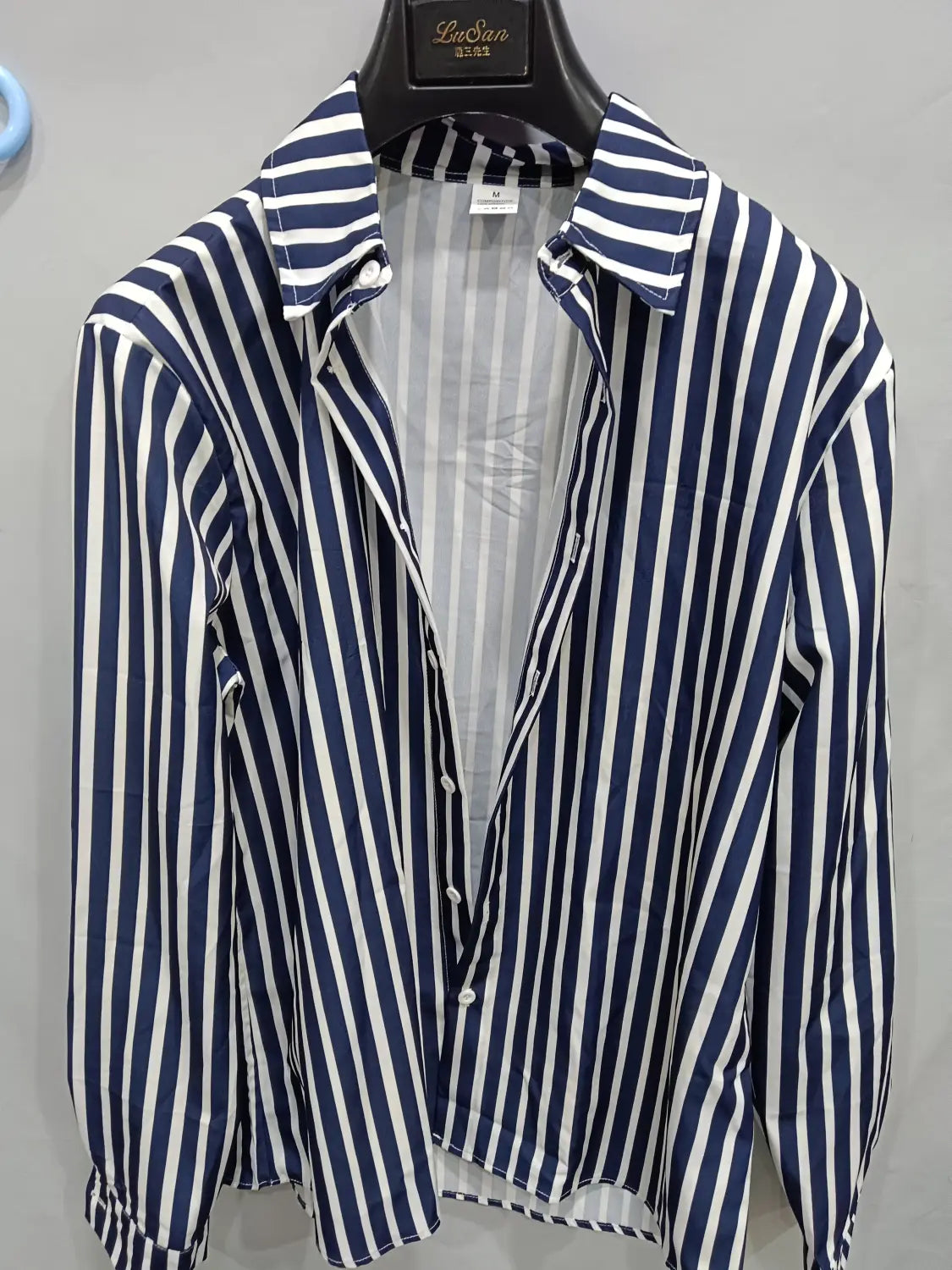 Chemise décontractée à manches longues rayée verticalement bleu marine et blanc pour hommes, avec col classique, suspendue sur un cintre noir.