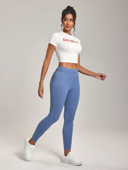 Weiße verkürzte T-Shirt mit roter Schrift und 'damn'-Schriftzug, kombiniert mit Jeansleggings mit hoher Taille, die als schlank machende Sporthose ausgelegt sind.