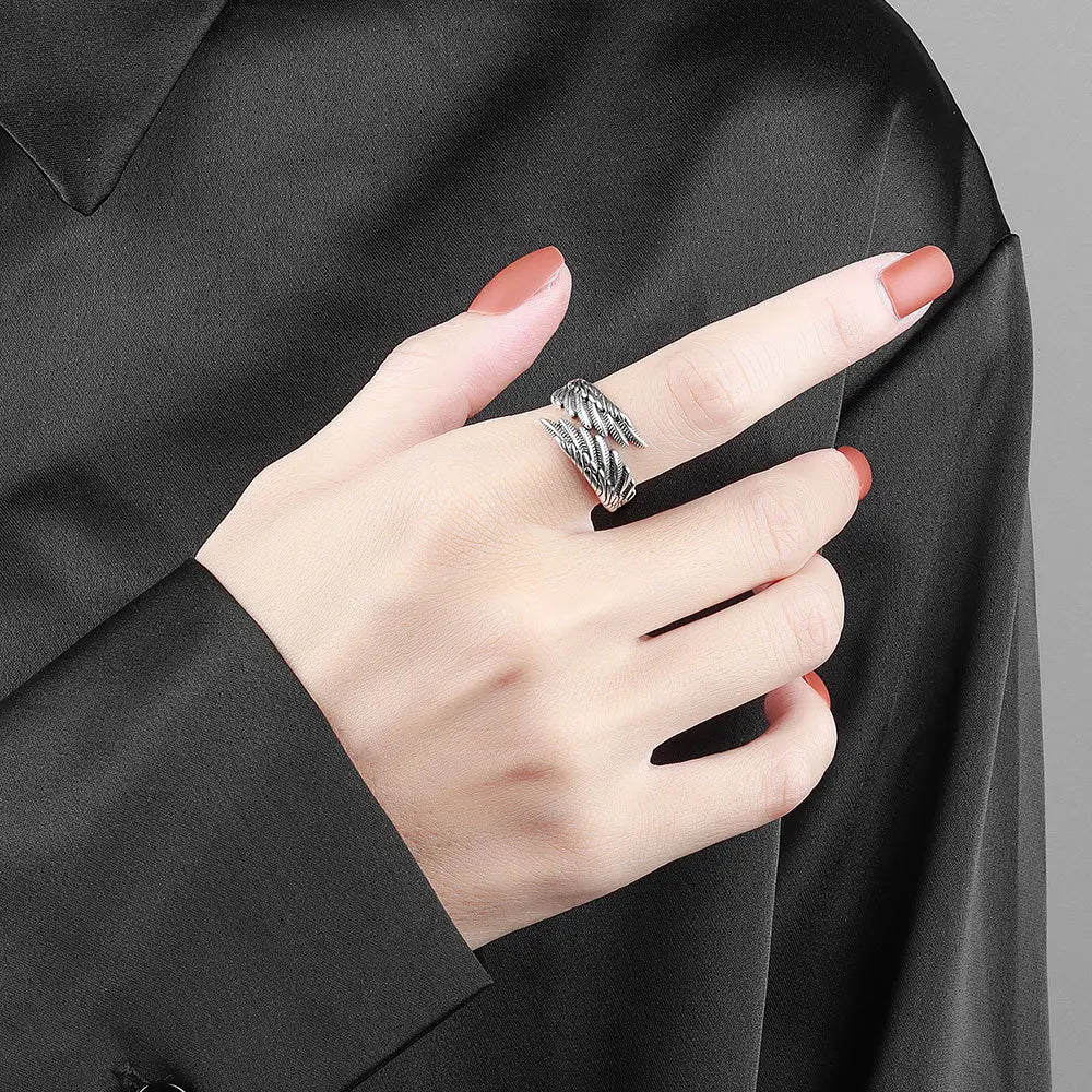 A sleek silver-toned 925 sterling silver detailed angel wing ring with an intricate feather design adorns the finger.