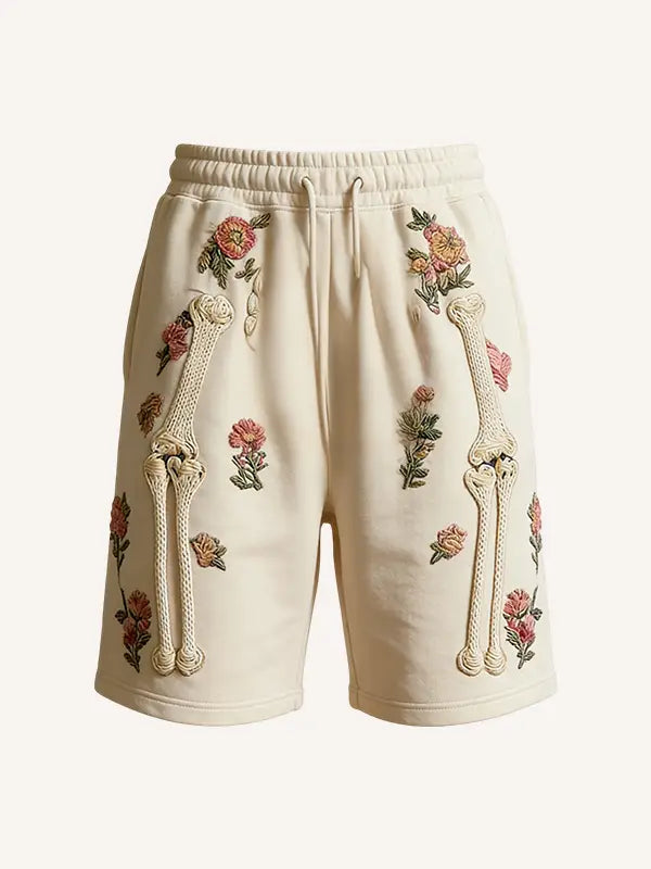 Cream-colored polyester sweat shorts embroidered with pink green and beige floral and bone designs for men titled Skeleton Floral Sweatshorts Embroidered Men Polyester.