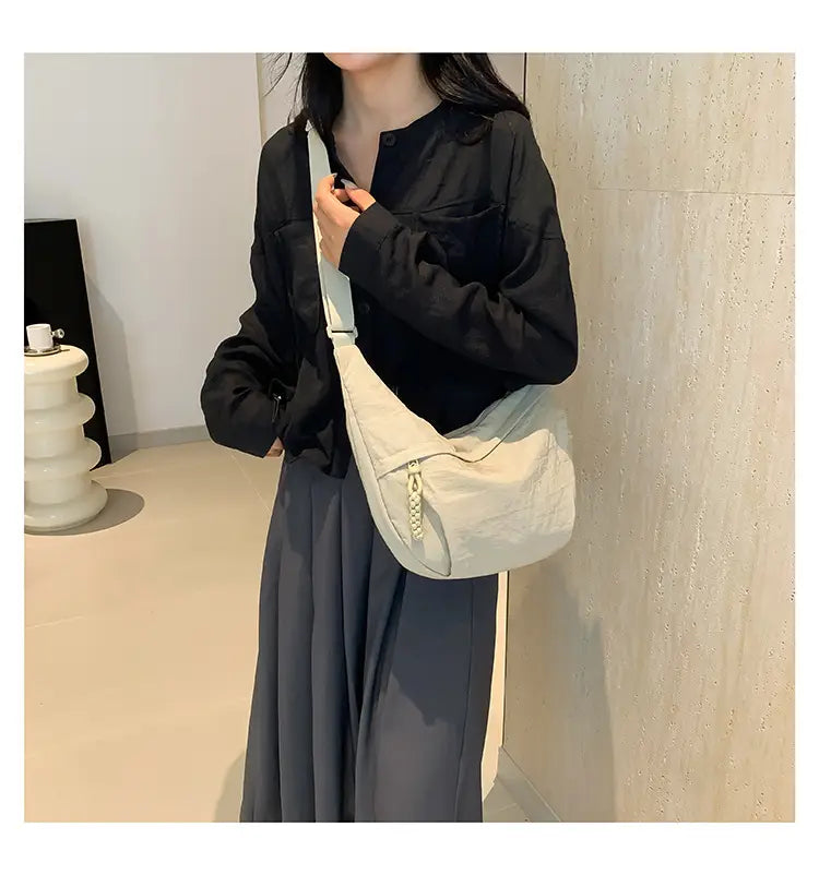 Cream-colored lightweight nylon crossbody bag with large capacity featuring a sleek zipper closure and adjustable strap for versatile shoulder use.