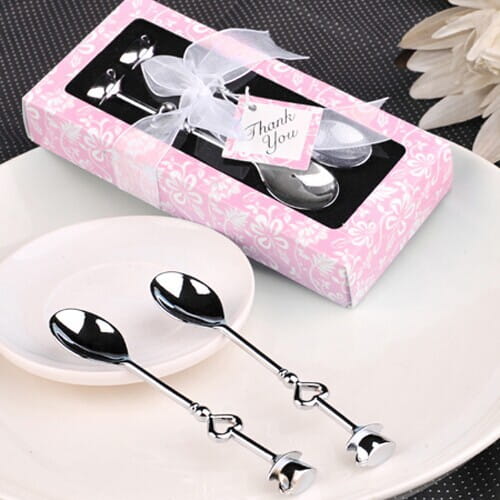 Silberfarbene Edelstahl-Kaffeelöffel in Herzform mit polierter Metalloberfläche, präsentiert in einer pinkfarbenen floralen Geschenkbox, gebunden mit einer weißen Schleife.