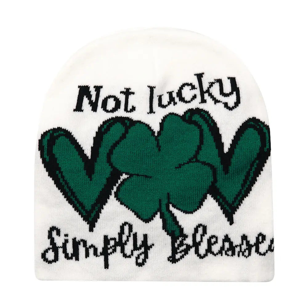 White knit beanie featuring a green shamrock design with black outlining and the text not lucky above and simply blessed below for a winter warm hat.