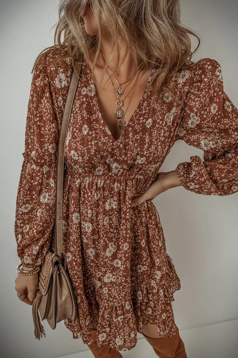 A flowing rust-colored floral print bohemian tiered mini dress with long puffed sleeves and a ruffled hem.
