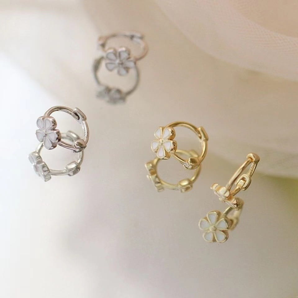 Silber- und goldfarbener Ohrhänger im Creolen-Look mit einer Daisy-Enamel-Blume sowie Clip-Ohrringen und Ohrsteckern mit zarten Vierblattblüten-Designs, die weiße Emaille-Zentren aufweisen.