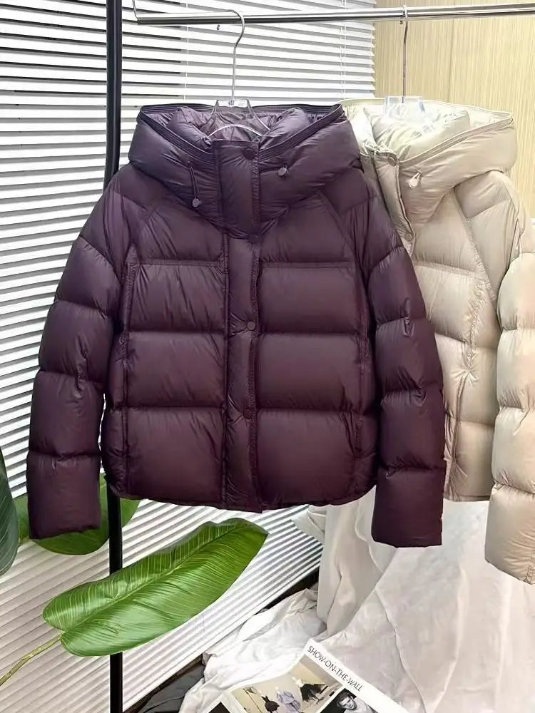 A dark purple quilted puffer jacket with a hood and front button closure designed as a loose hooded winter coat.