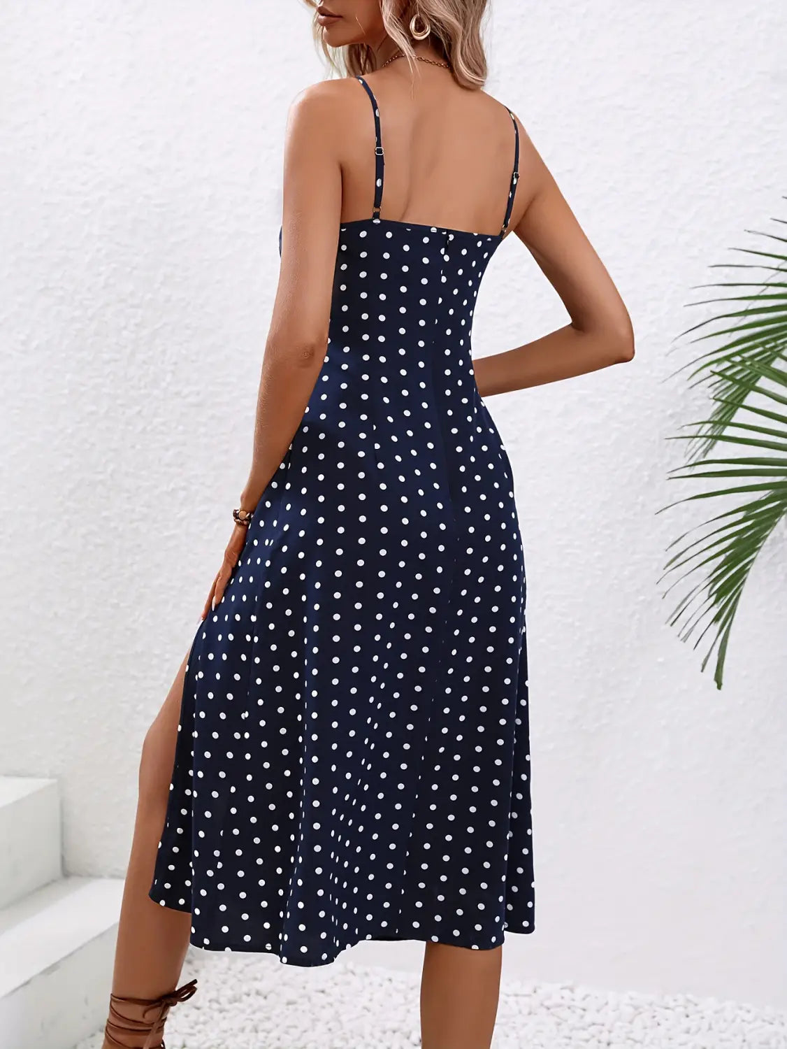 A navy blue midi dress with white polka dots and thin spaghetti straps featuring a side split.