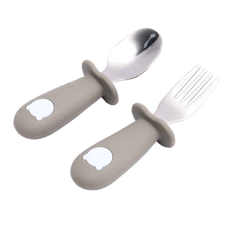 Ensemble cuillère et fourchette pour bébé à manches en silicone gris, avec des têtes en acier inoxydable, présentant un motif de tête d’ours blanc sur chaque manche.