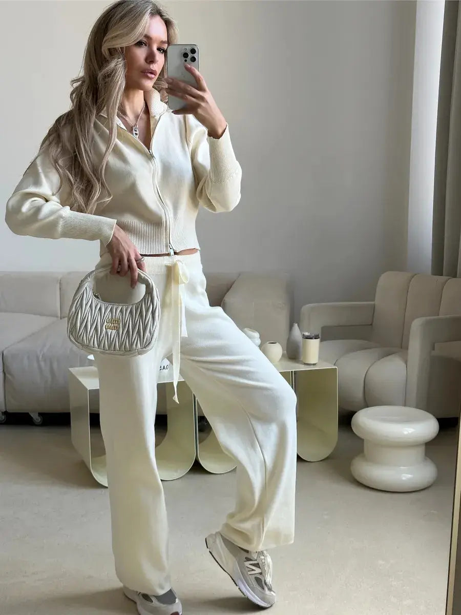 A cream-colored quilted handbag with a structured rounded shape and top handle complementing a women’s knit zip up cardigan and wide leg pant set.