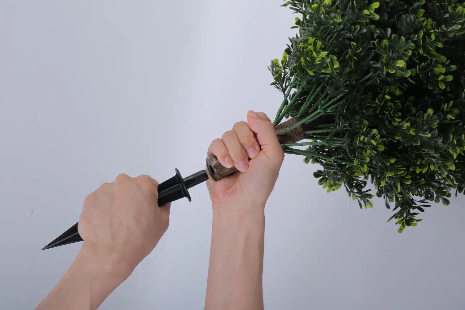 black plastic garden spike with a textured wooden handle used to plant an artificial green bush from artificial boxwood ball topiary trees with spikes 2 pack