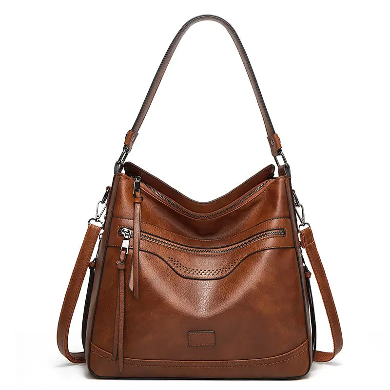 Vintage-Ledertasche im Totebag-Stil in Braun mit mehreren Reißverschlussfächern, einem gebogenen oberen Tragegriff, einem verstellbaren Crossbody-Riemen und dezenten perforierten Details.