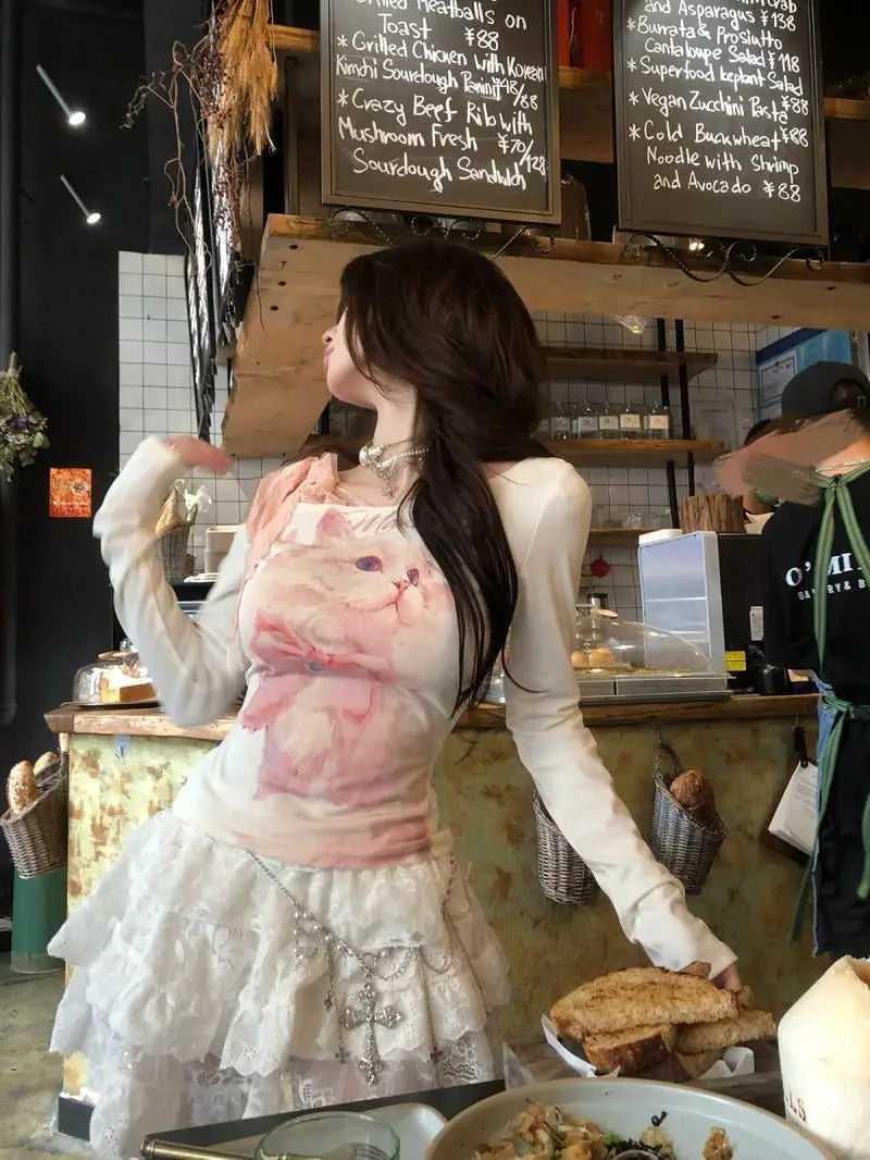 White long-sleeved lace halter top featuring a pink cat graphic and ruffled skirt detail.