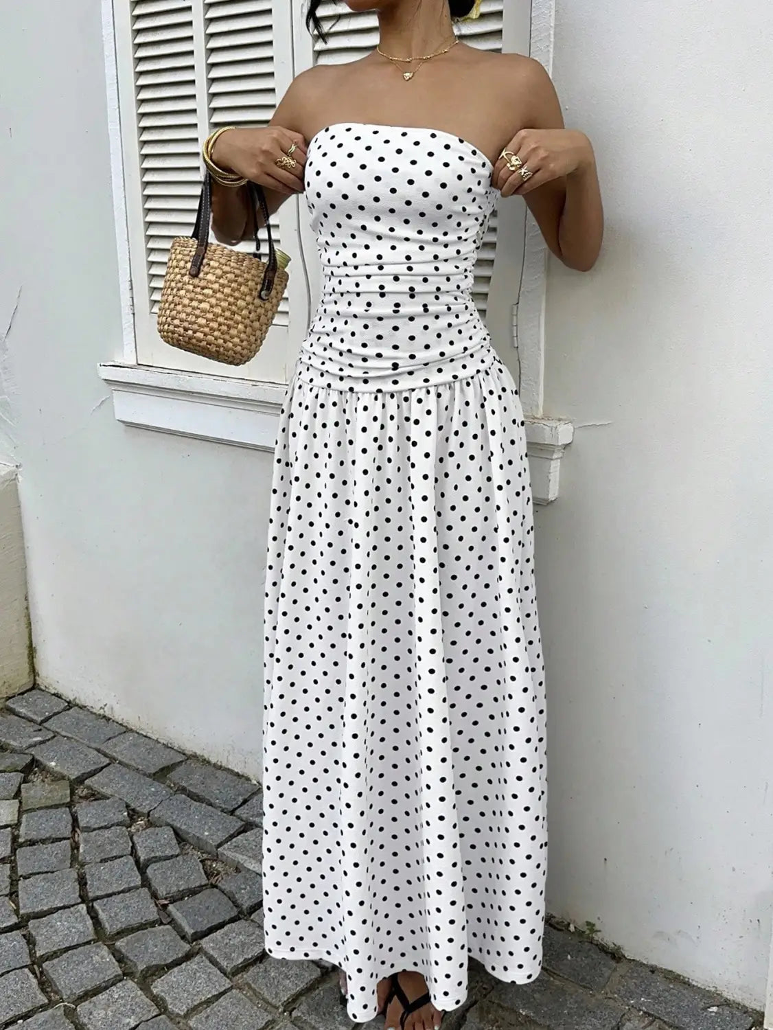 White strapless maxi dress with black polka dots and a ruched waist designed as a polka dot off shoulder strapless maxi dress.