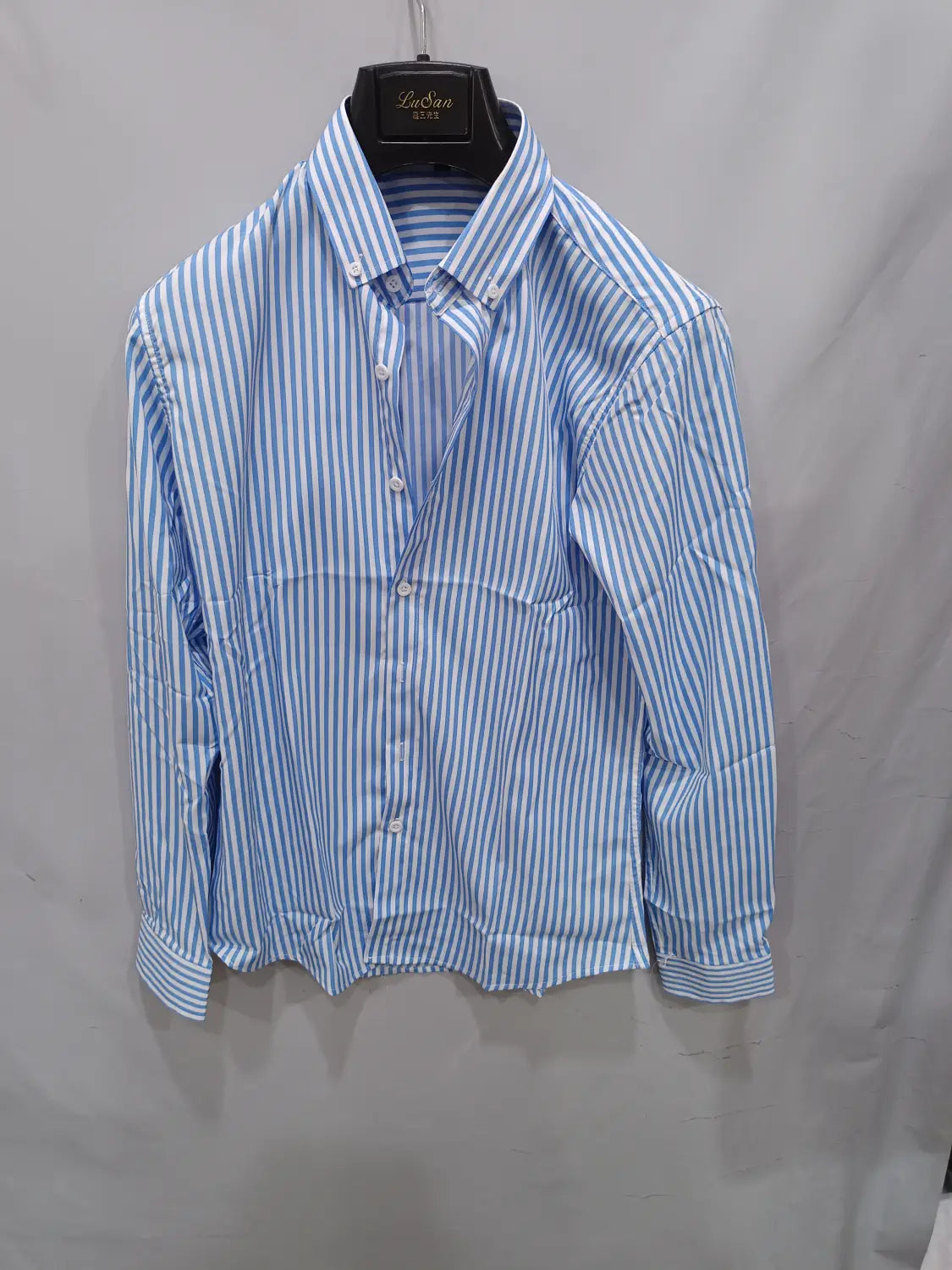 Chemise décontractée à manches longues rayée verticalement bleu clair et blanc pour hommes, suspendue sur un cintre noir.