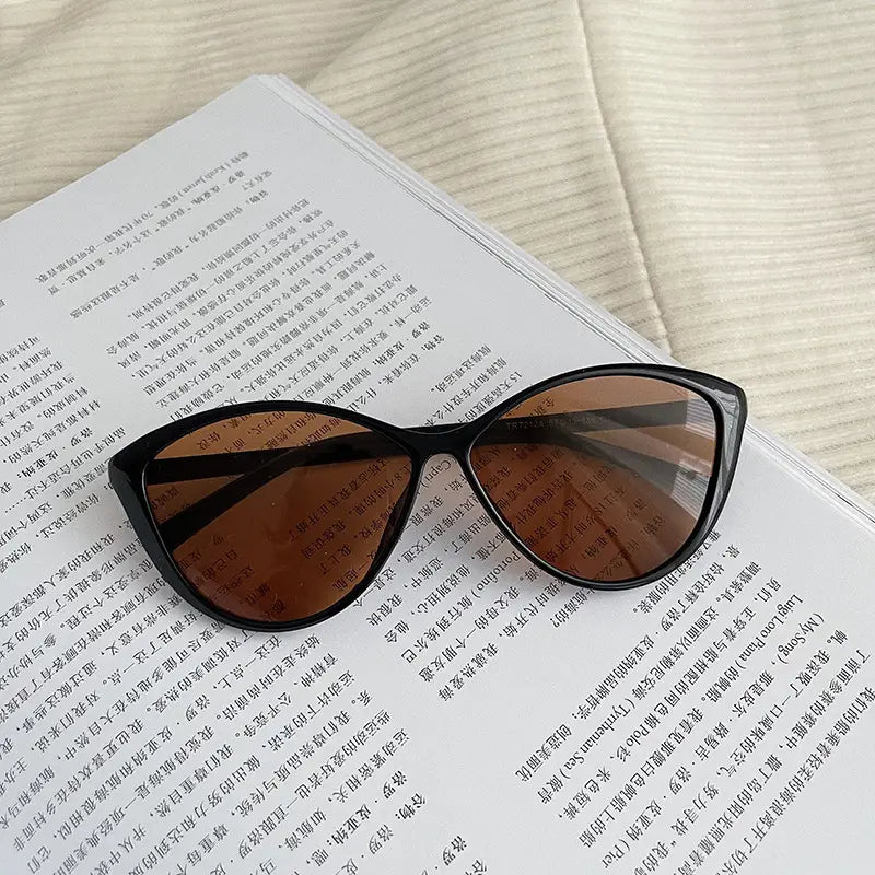 Lunettes de soleil œil-de-chat noires avec des verres teintés marron, offrant une protection rétro UV380 et un design léger pour la mode.