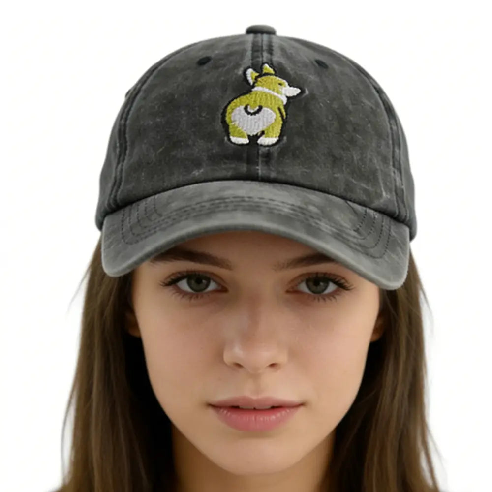 Une casquette de baseball en denim gris terne vieilli, avec un motif de corgi vert et blanc brodé à l’avant.