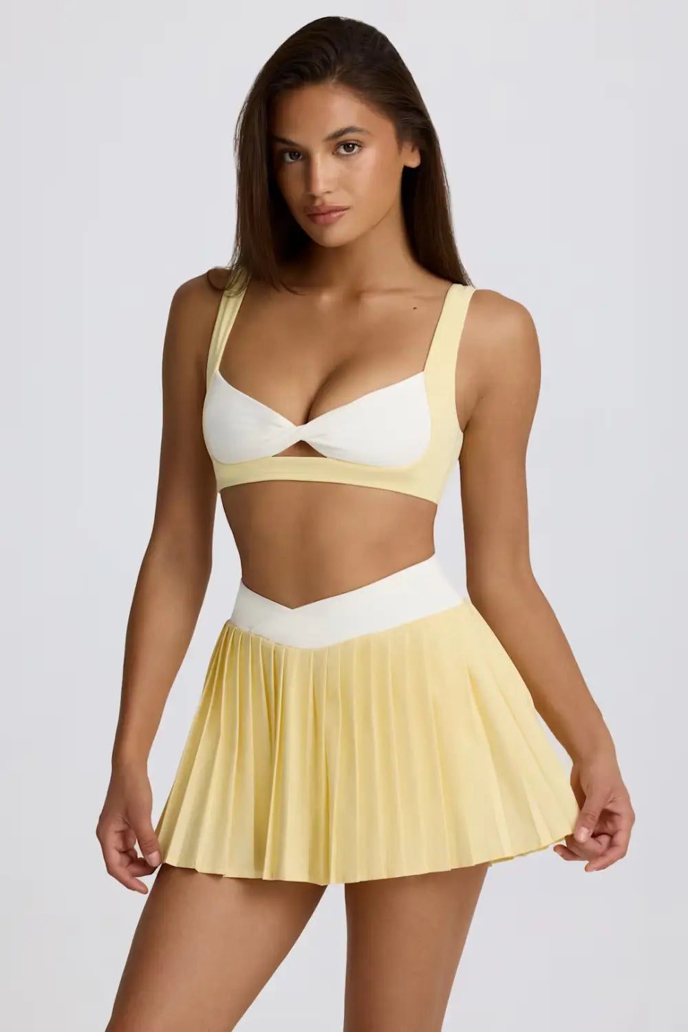 Zweiteiliges Sportoutfit mit einem Bikini-Top in Weiß und Hellgelb mit Cut-out-Details sowie passendem plissiertem, figurformendem Fitnessrock.