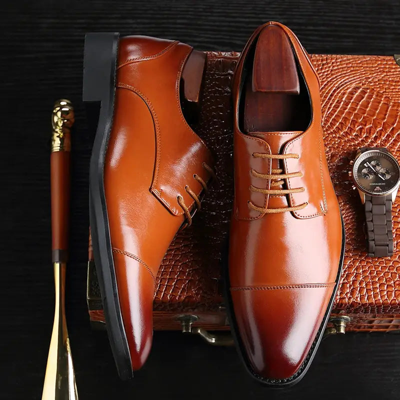 Herren-Businessschuhe im britischen Stil mit spitz zulaufender Zehenpartie aus poliertem braunem Kunstleder mit Kappenzehe und passenden Schnürsenkeln zur geschäftlichen Verwendung.