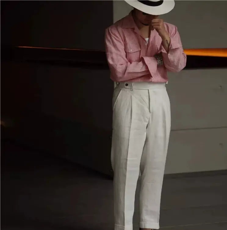 A man wearing high waisted white linen trousers and a pink button up shirt.