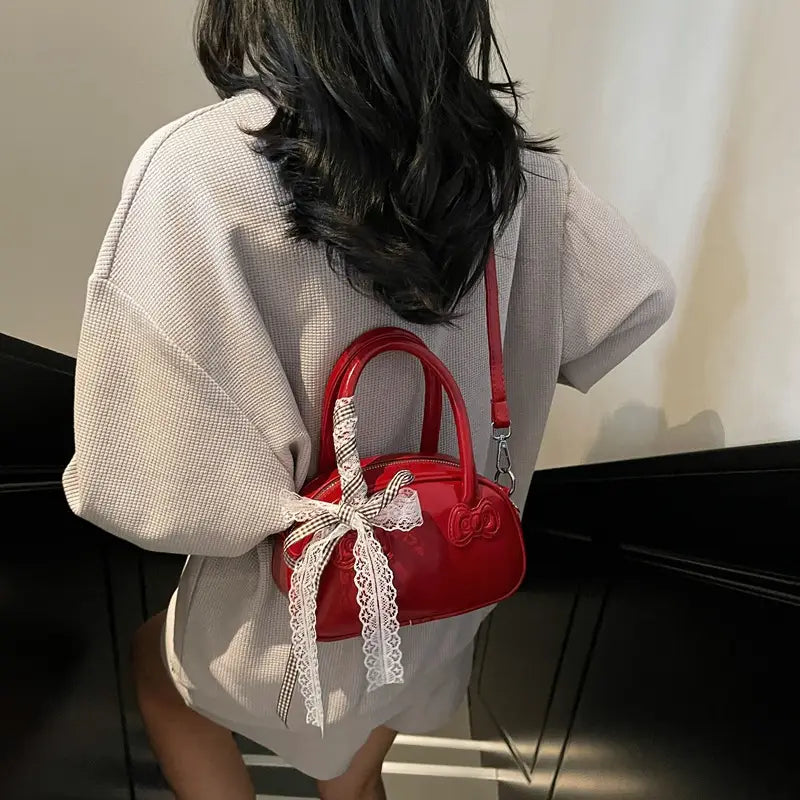 A glossy red Hello Kitty crossbody bag with a white lace bow and matching shoulder strap.