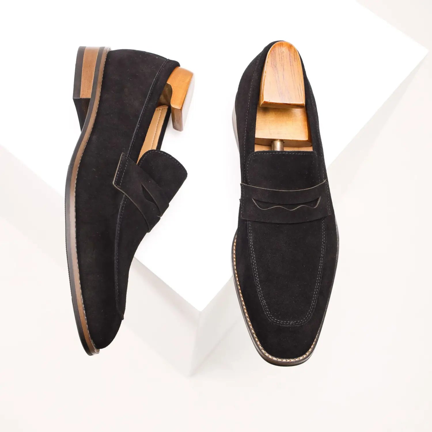Black suede penny loafers for men with contrasting tan stitching and wooden shoe trees for support in a classic casual leather shoe design.