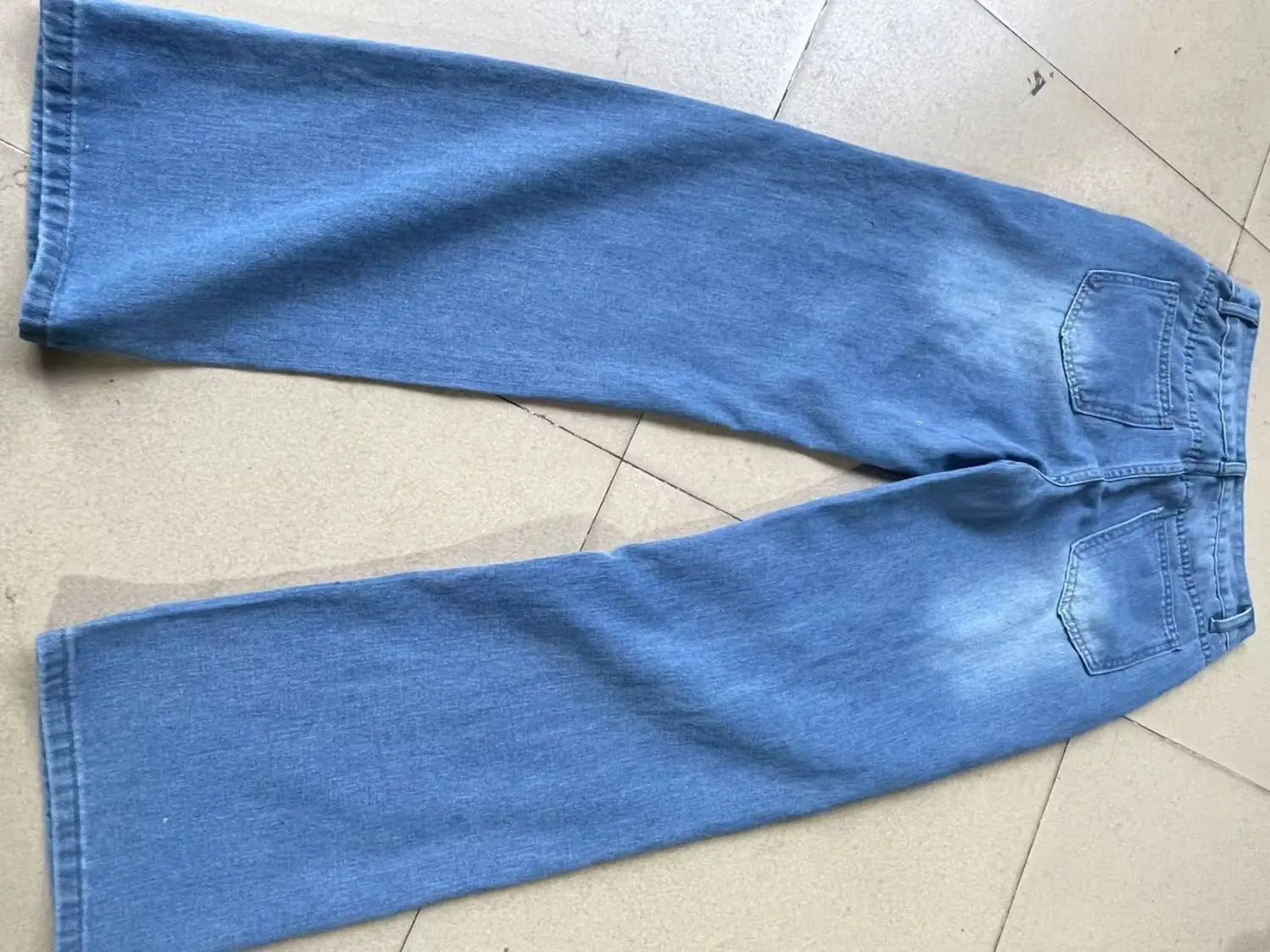 distressed high rise wide leg denim jeans in light wash blue with a straight-leg cut and classic back pockets shown from the back side.