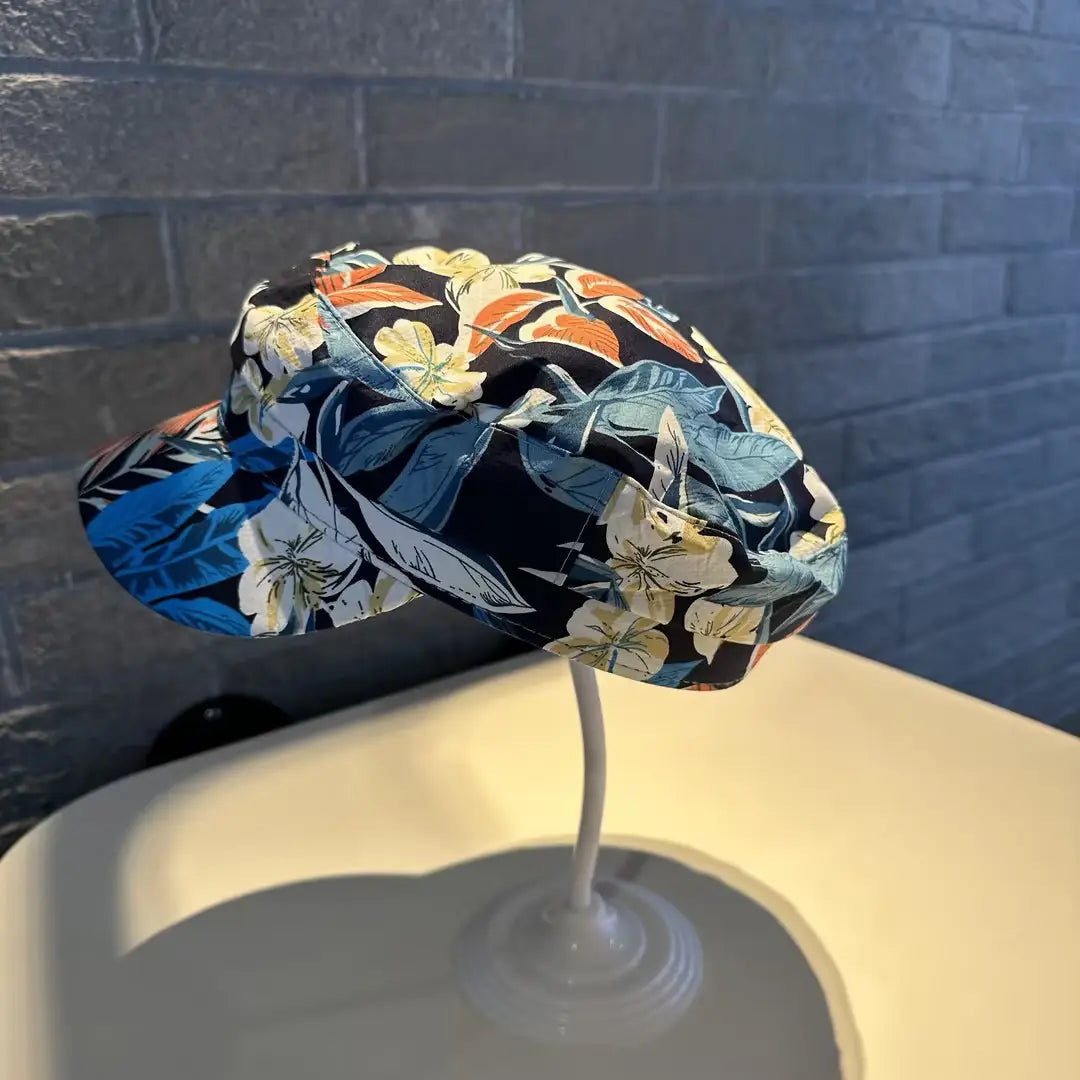 Gorra tipo bucket hat floral, estilo coreano, impresa, con flores vibrantes en azul, naranja y blanco sobre una tela azul marino oscura.