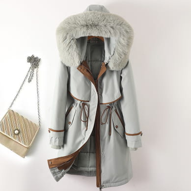 Hellgraue Damen-Winterfelljacke mit Kapuze und wattierter Polsterung mit plüschigem, hellfarbenem Fellfutter sowie braunem Lederzierbesatz an Ärmelbündchen, am Taillenbund und an den Taschen.