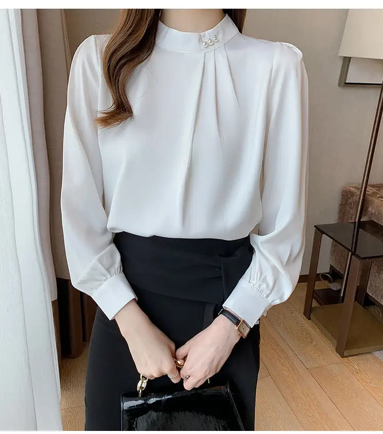 Blouse en satin blanche pour femmes, avec un col haut et des accents de boutons perle sur un ajustement ample.