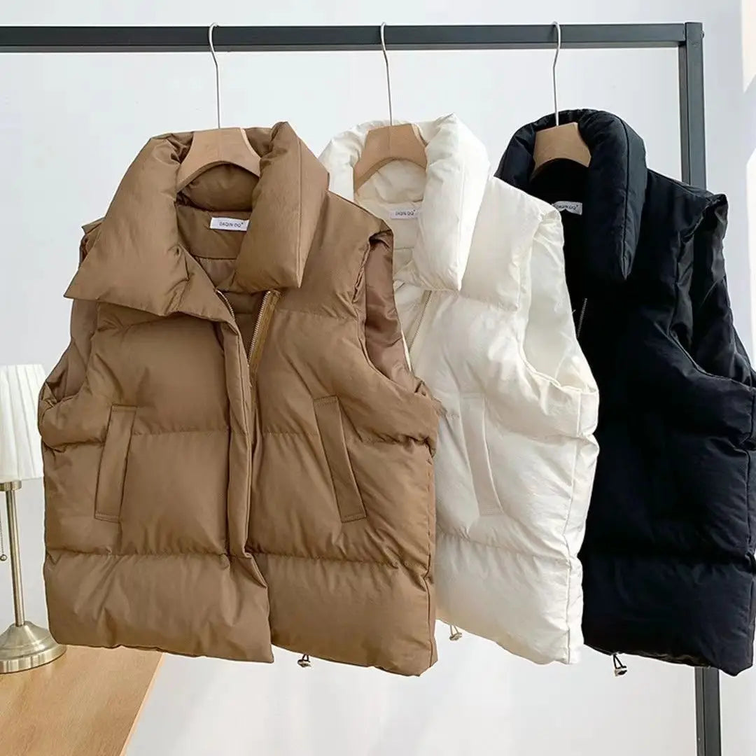 Three women quilted puffer vests in tan white and black hang on a rack showcasing loose sleeveless outerwear.