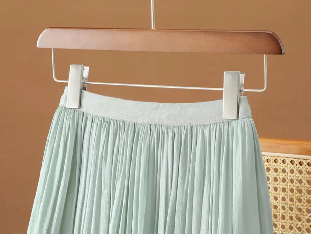 Ein sanftes mintgrünes, irrisierendes Chiffon-Faltenrock mit elastischem, dehnbaren Bund, der an einem Holzkleiderbügel hängt.