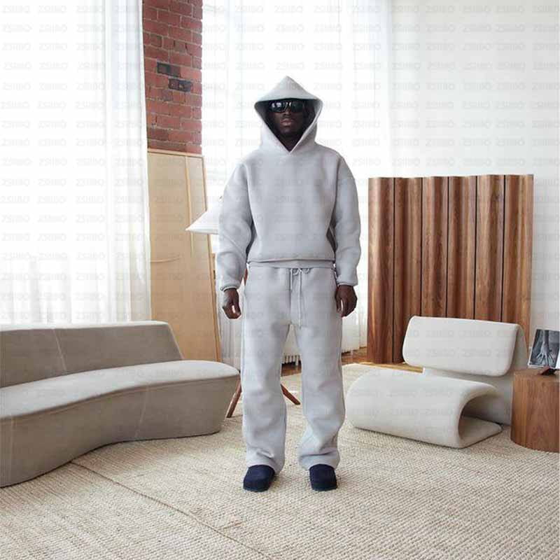 Une personne portant un sweat à capuche oversize unisexe streetwear gris clair, avec un cordon de serrage, et un pantalon de survêtement assorti fabriqué dans un tissu doux en mélange de coton.