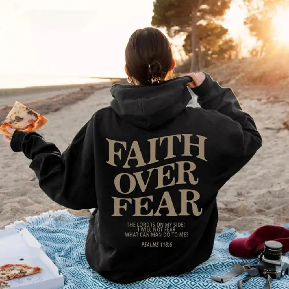 Black hoodie shown from the back with faith over fear printed in beige lettering and psalms 118 6 biblical verse below in a christian aesthetic design.