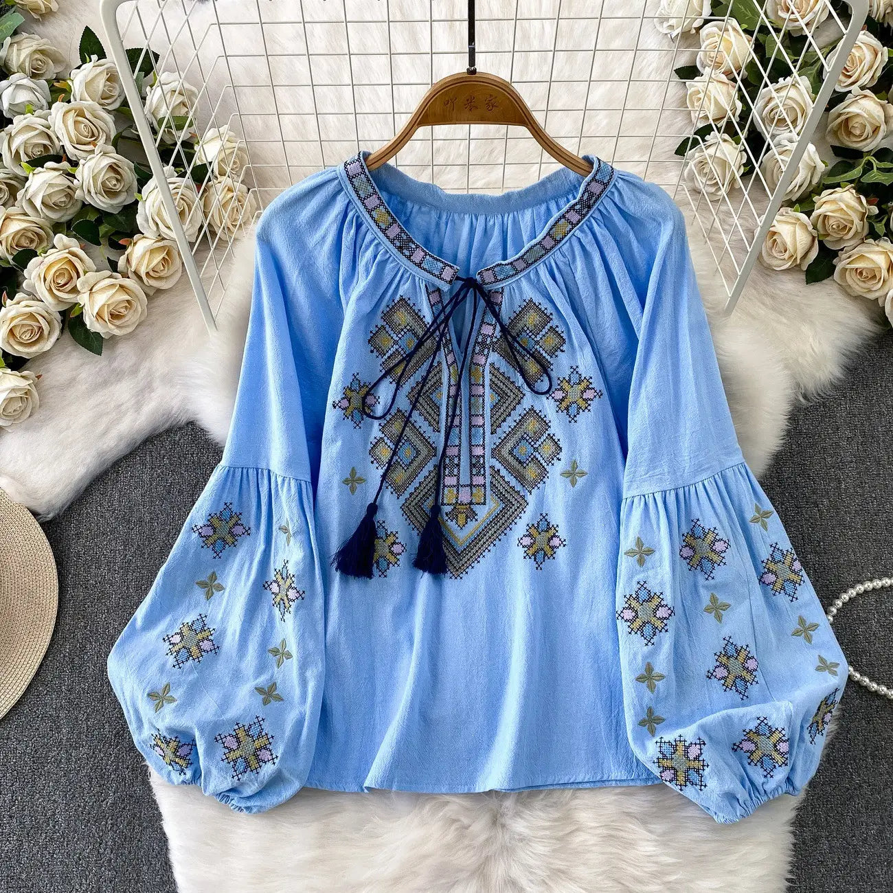 Light blue embroidered blouse with long puffed lantern sleeves and a decorative tie neck featuring dark tassels.