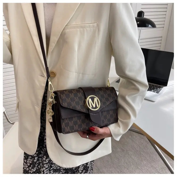 Dark brown monogram letter print crossbody messenger bag with a repeating pattern and a gold-tone circular m clasp.