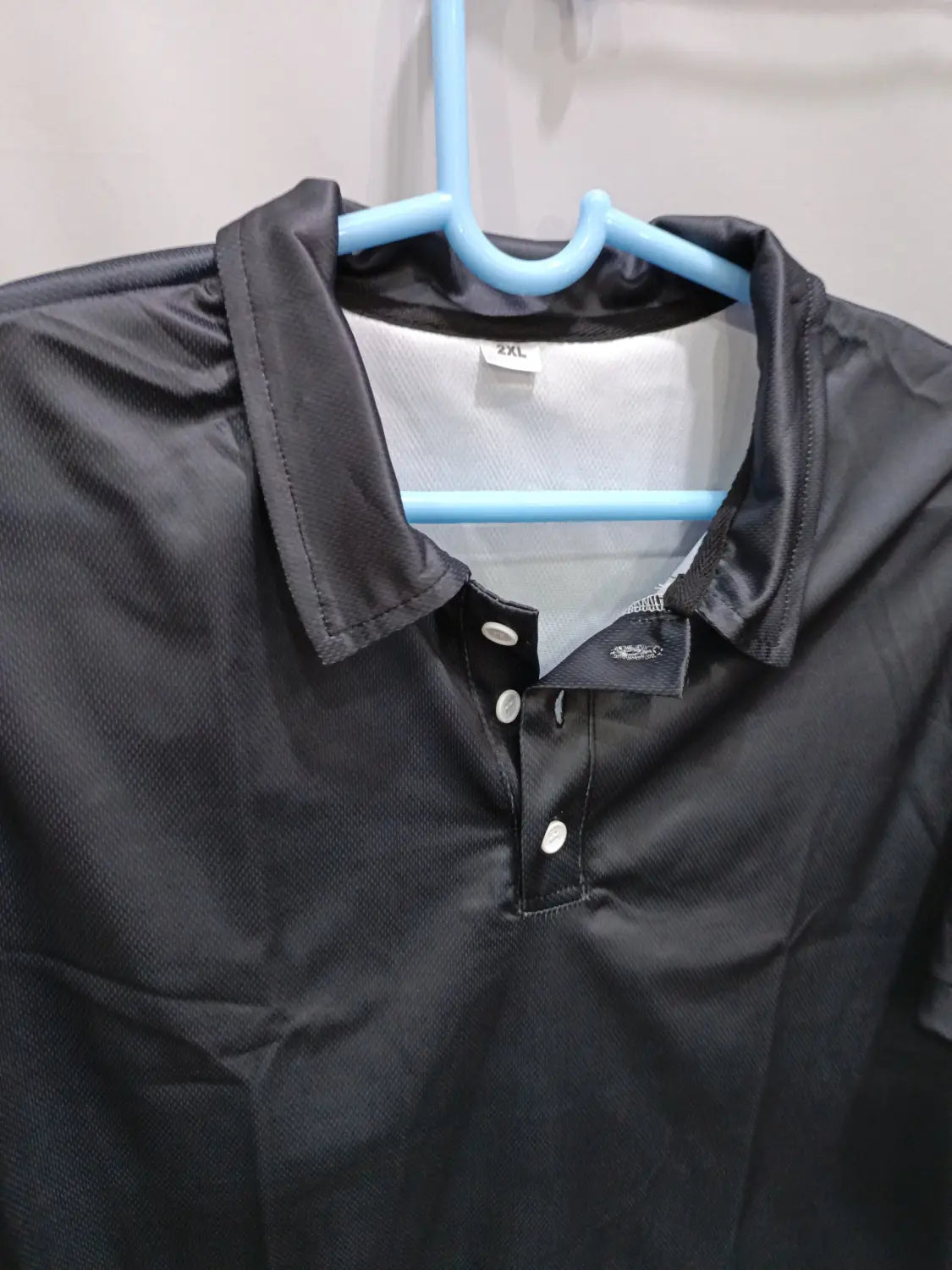 Herren-Cardigan mit kurzer Ärmellänge, strukturiert, mit Knopfleiste, schwarz, mit Kragen und weißen Knöpfen, die an einem blauen Bügel hängen.