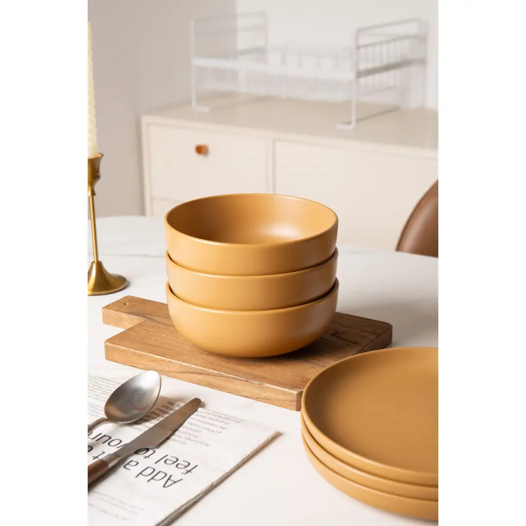 Stack of matte mustard-yellow stoneware ceramic bowls from a 12 piece dinnerware set with matte glaze for four.