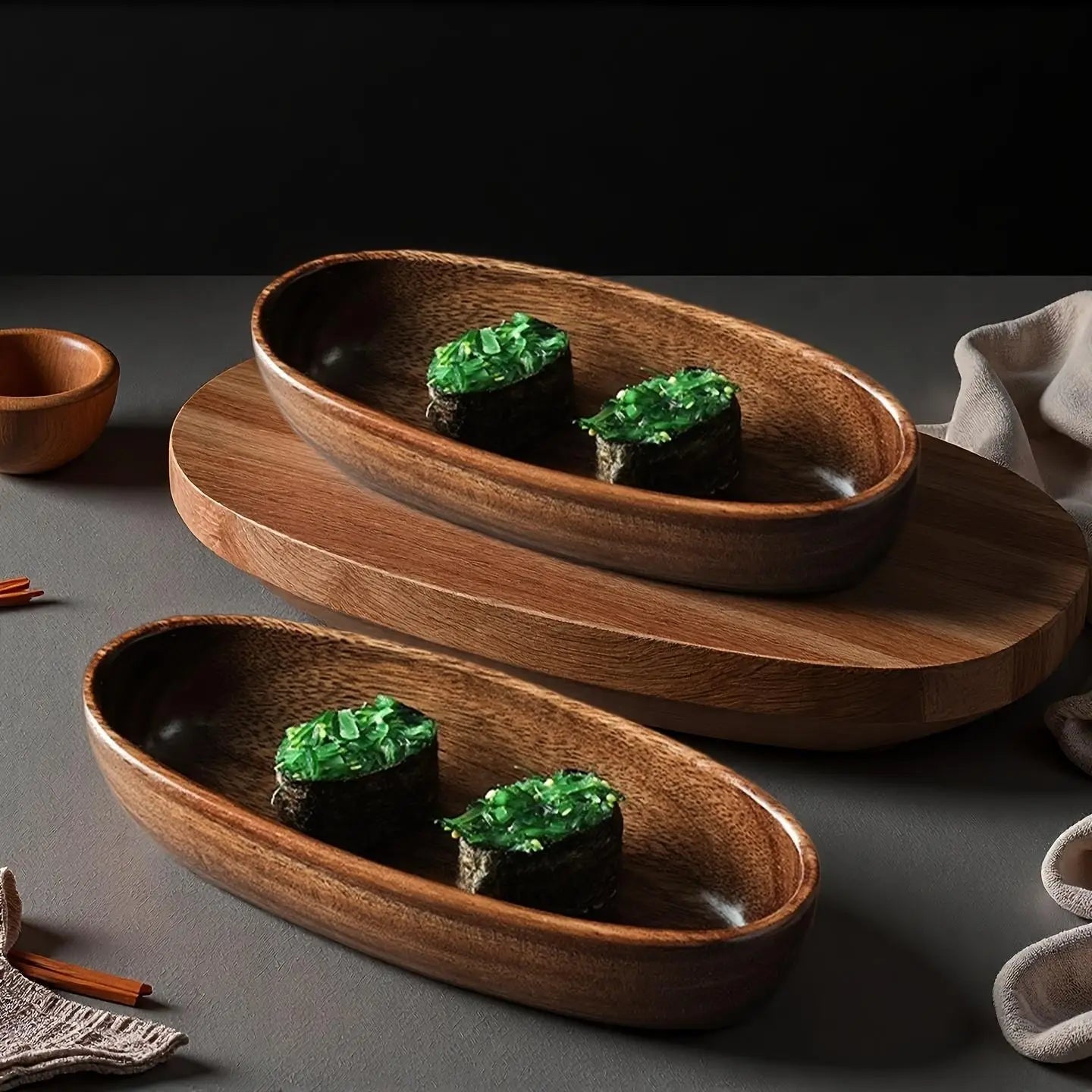 Dos bandejas de madera artesanales con forma ovalada en un acabado natural, cada una con dos piezas de sushi coronadas con guarnición verde, como parte de un set de barco de madera para sushi japonés.