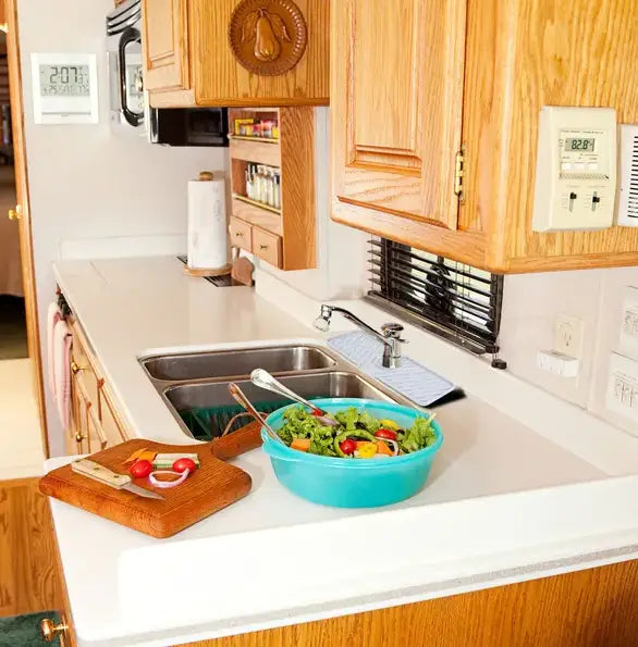 Un saladier en plastique turquoise éclatant, rempli de jeunes pousses et de légumes aux couleurs variées, placé sur un tapis de robinet en silicone pour évier de cuisine, pare-éclaboussures, avec plateau de drainage.