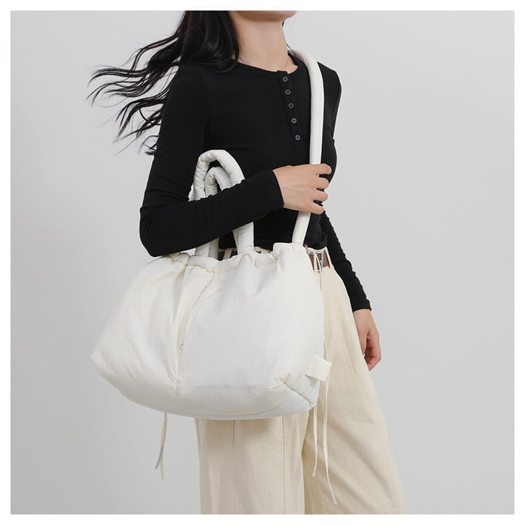 White quilted puffer tote bag made of lightweight nylon with plush quilted handles and a drawstring closure designed as a shoulder bag.