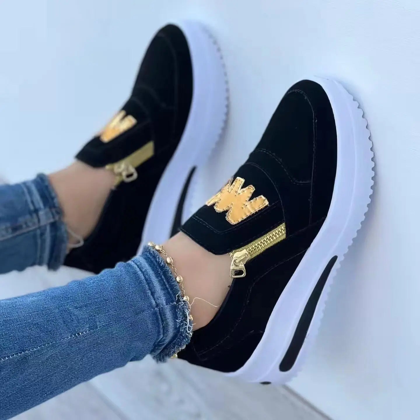 Baskets compensées à enfiler pour femmes en daim noir, avec accents de fermeture éclair ton sur ton doré et semelle plateforme blanche.